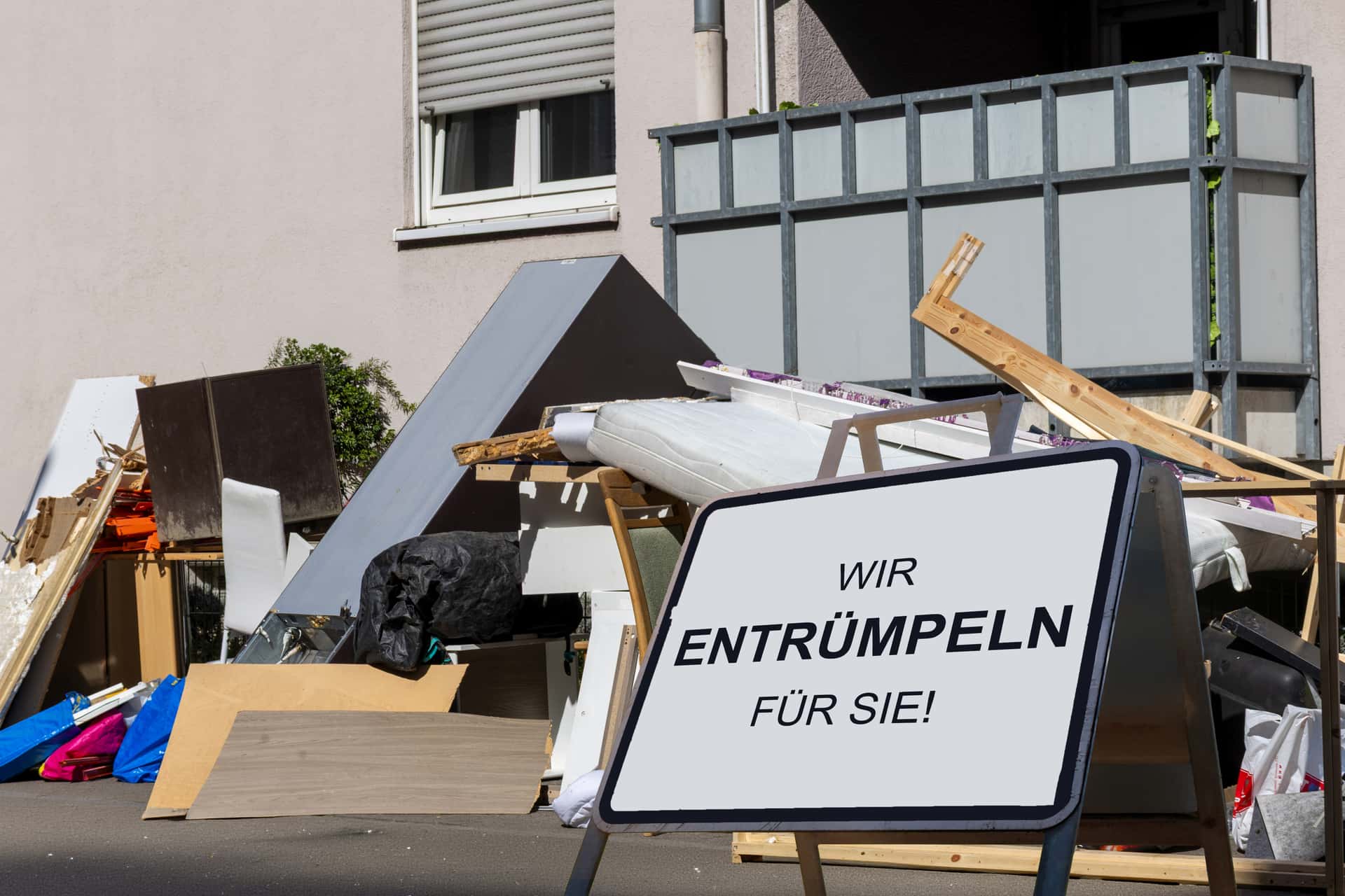 Entrümpelung: Sperrmüll vor einem Mehrfamilienhaus Sperrmüll und alte Möbel vor einem Mehrfamilienhaus mit Schild Wir entrümpeln für Sie von KOMMZE MA EBEN
